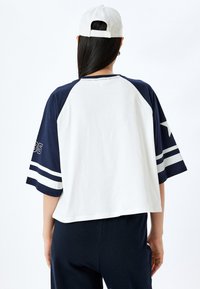 Camiseta estilo béisbol blanca y azul marino con mangas raglán cortas, con una estrella y el número 35 en las mangas, fabricada en suave algodón.