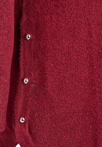 Bordo kardigāns ar mīkstu, teksturētu adījumu. Iekļauti sudraba pogas uzmalē aizdarei. Tuvplāns par auduma tekstūru.