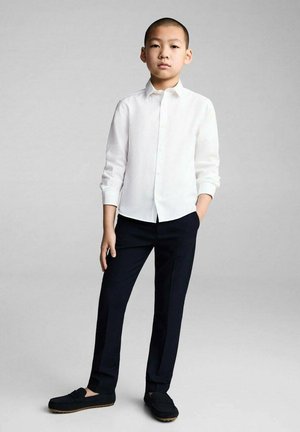 Chemise blanche à manches longues et à boutons, pantalon noir ajusté et mocassins foncés. Design simple avec une coupe ajustée, style minimaliste et texture lisse.