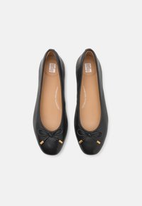 Ballerines en cuir noir avec des orteils ronds, présentant un nœud à l'avant et des accents dorés. Les semelles intérieures sont de couleur beige clair, avec une texture lisse.