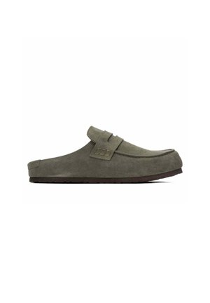 Zapato mule de ante gris tipo slip-on con suela plana marrón y una tira decorativa en la parte superior delantera.