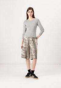 Grå genser med perle detaljer, sammen med kne-lange shorts med slangeskinnmønster i beige og brunt. Svarte joggesko med hvite striper fullfører antrekket.