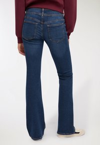 Ciemnoniebieskie dżinsy w kształcie dzwonów z wysokim stanem, pięcioma kieszeniami i jasnymi przeszyciami. Gładka faktura z niewielką elastycznością.