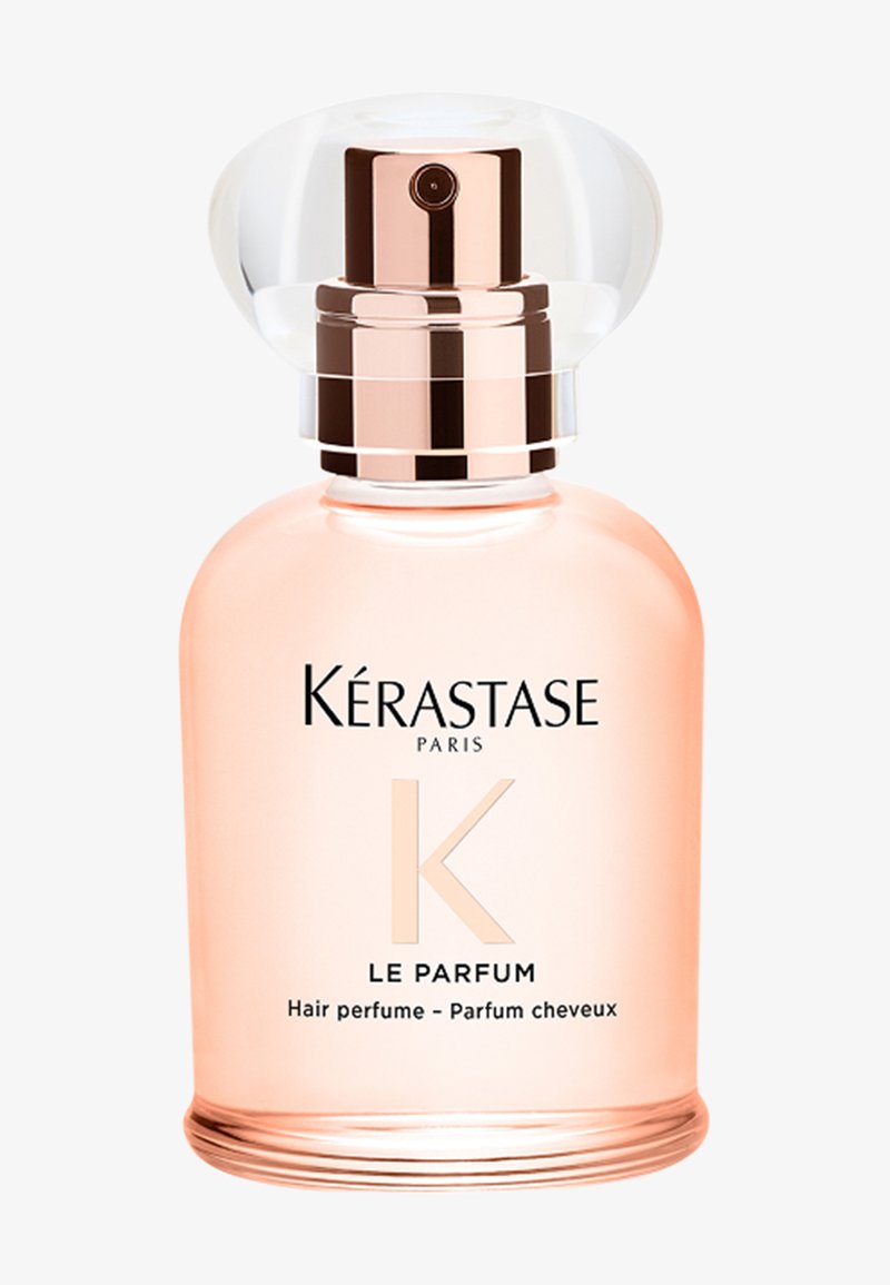 Kérastase Paris Le Parfum, perfume capilar en una botella de vidrio transparente con una tapa redondeada y transparente. Líquido rosa visible, con texto en plata y negro.