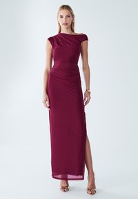 Bordeaux Abendkleid mit asymmetrischem Design, drapiertem Stoff, seitlichem Schlitz und bodenlanger Silhouette. Glatte Textur, minimaler Zierrat.
