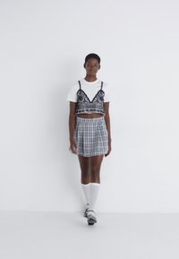 Top corto de estampado blanco y negro superpuesto sobre una camiseta blanca, combinado con una falda de cuadros y calcetines altos blancos.