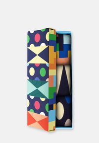 Geschenkbox mit auffälligen geometrischen Mustern in lebhaften Farben, die zusammengerollte Socken in verschiedenen Farben und Mustern enthält, vor einem weißen Hintergrund präsentiert.