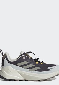 Chaussure de randonnée Adidas Terrex Gore-Tex noire et grise avec une semelle blanche épaisse et des accents jaunes sur les lacets, sur un fond gris clair.