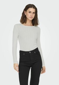 White ribbed long-sleeve top with a round neckline, paired with high-waisted black jeans featuring front pockets and metal hardware.