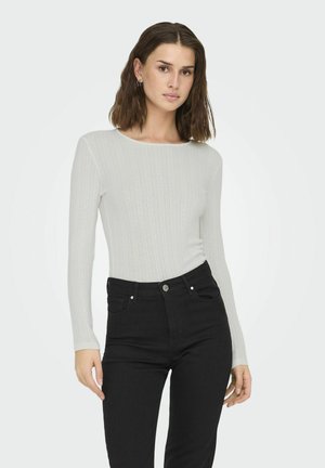White ribbed long-sleeve top with a round neckline, paired with high-waisted black jeans featuring front pockets and metal hardware.