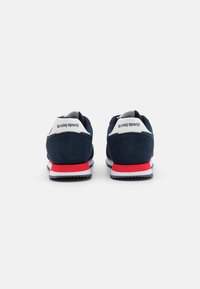 Scarpe sportive in suede blu navy con accenti bianchi e rossi, caratterizzate da una suola stratificata e un logo sul tallone. Vista posteriore mostrata.