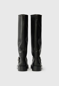 Botas de couro pretas até ao joelho com uma textura suave, uma silhueta esbelta e um salto bloco. Apresentam um detalhe de fivela na lateral.