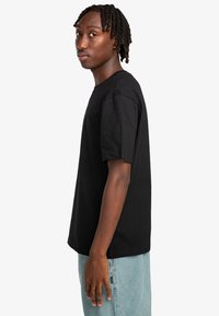 Black cotton t-shirt with short sleeves, crew neck design, relaxed fit, displayed from the side against a plain white background.