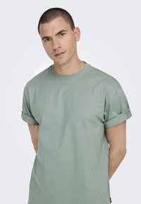 Groen T-shirt met korte mouwen en omgeslagen mouwen, gemaakt van zacht katoen. Heeft een ronde hals en een comfortabele pasvorm.