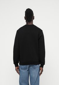 Juodas džemperis su apvalia apykakle, ribinėmis rankovėmis ir apačia. Dėvimas su šviesiai mėlynais džinsais, rodančiais laisvą siluetą ir minkštą tekstūrą.