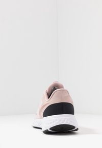 Pinkfarbener Sportschuh mit glattem synthetischem Obermaterial, schwarzem Mittelfußakzent und strukturiertem weißen Laufsohlenprofil mit Noppen für besseren Grip.