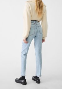 Höga ljusblå jeans med rak bendesign, med bakfickor och enkelstickning, tillsammans med en krämfärgad tröja och svarta skor.