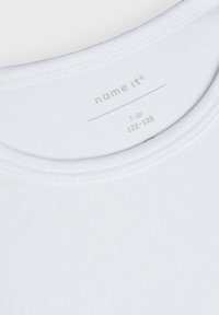 T-shirt en coton blanc avec un col rond et une texture douce et lisse. Étiquette d'entretien visible avec le nom de la marque et les détails de taille.