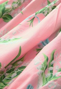 Růžová látka s květinovým vzorem, na které jsou bílé konvalinky a zelené listy. Textura je hladká a mírně lesklá.