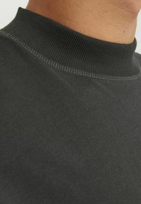 Črna, prilegajoča se turtleneck pulover z rebrasto teksturo in šivnim detajlom okoli ovratnika, ki prikazuje bližnji posnetek zgornjega dela vratu.