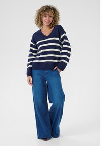 Maglione oversize a righe blu navy e bianche con scollatura a V e polsini a coste, abbinato a jeans a gamba larga blu. Vestibilità rilassata e texture morbida.