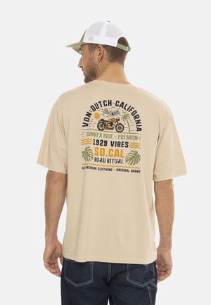 Camiseta de algodón beige con un corte relajado. La impresión gráfica en la parte posterior presenta una motocicleta, palmeras y texto en varios colores. Mangas cortas.