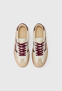 Hvite og beige sneakers med burgunder detaljer, snørebånd og en teksturert semsket overflate. Har rund tå og gummisåle.
