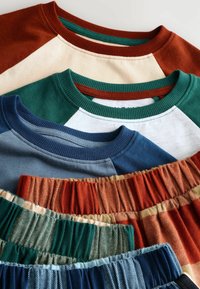 Cinco camisetas de varios colores: óxido, crema, azul verdoso, azul marino y tela estampada con pliegues; algodón o material similar; escotes redondeados.