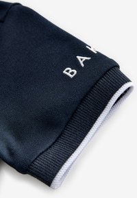 Mouwboord in marineblauw met geribbelde breistructuur en witte geborduurde letters "B A" die gedeeltelijk zichtbaar zijn bij de rand met witte rand.