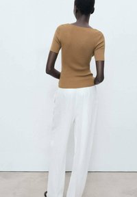 T-shirt marron côtelé à manches courtes associé à un pantalon plissé blanc. Le haut a un col bateau et une silhouette ajustée, mettant en valeur une texture douce.
