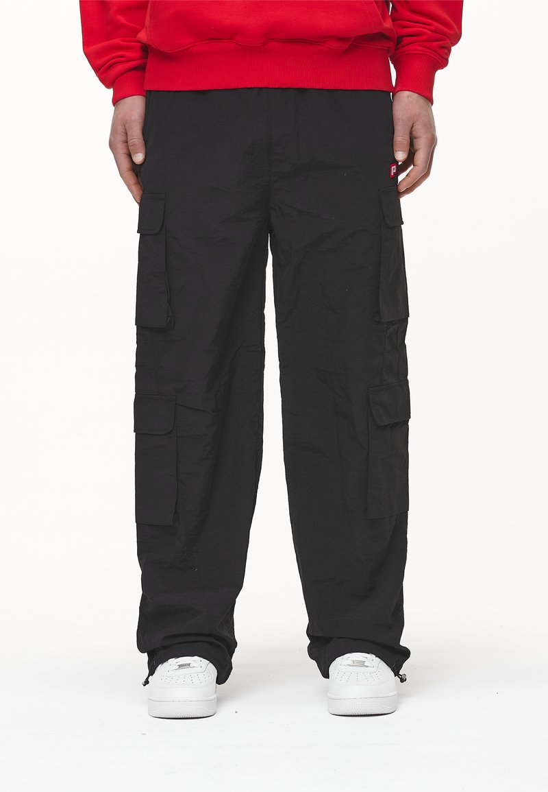 Pantaloni cargo negri cu multiple buzunare laterale, fabricați dintr-un material texturat. Asortați cu adidași albi și un hanorac roșu.