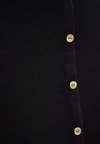 Vêtement en maille côtelée noire avec une rangée de cinq boutons dorés sur le devant, offrant un aspect texturé avec une coupe ajustée.