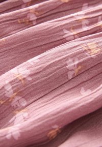 Blødt, pink stof med en struktureret vævning, der har et subtilt blomstermønster i lysere nuancer. Den plisserede design tilføjer dybde.