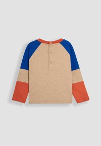 Pitkähihaisessa T-puserossa on beige vartalo ja siniset, oranssit sekä punaiset raglanhihot. Selässä on nappilista. Puuvillamateriaali.
