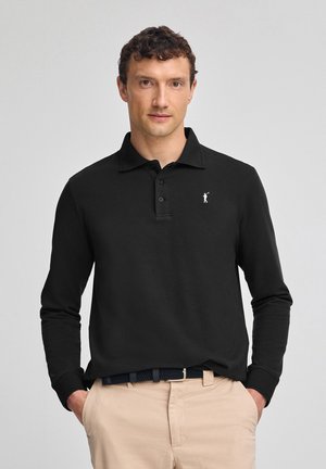 Camisa polo negra de manga larga con cuello, que presenta una tapeta con tres botones y un pequeño logo blanco bordado en el lado izquierdo del pecho.
