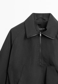 Maglione nero con cerniera frontale, colletto ampio e dettagli sulle cuciture laterali. Realizzato in un tessuto liscio con un design minimalista.