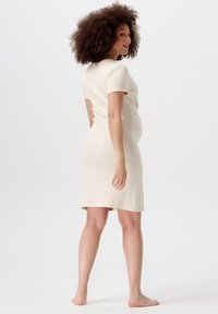 Beige kortärmad klänning med en figurnära silhuett, mjuk textur och knälång nederkant. Inga synliga mönster eller hårdvarudetaljer.