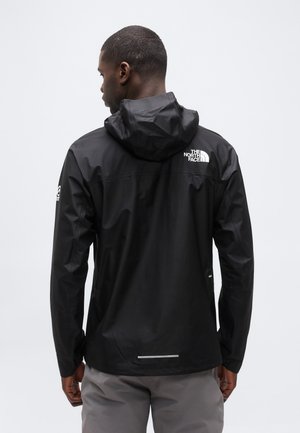 Mann trägt eine schwarze wasserdichte The North Face Jacke mit Kapuze, von hinten vor einem schlichten hellen Hintergrund gezeigt.