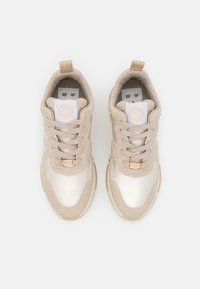 Beżowe sneakersy z gładką syntetyczną i zamszową cholewką, sznurowanym designem, okrągłym noskiem oraz naszywką z logo na języku.