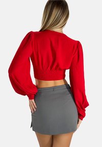 Crop top rosso con maniche a sbuffo e vita arricciata, abbinato a una mini gonna grigia con spacco laterale.