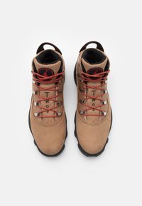 Paire de baskets montantes beige et noires avec des lacets rouges, une texture en mesh, et le texte « Two 3 » sur la languette, vues de dessus sur fond blanc.