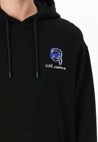 Felpa nera con cappuccio e coulisse, caratterizzata da un design ricamato colorato di un volto con occhiali da sole e il testo "KARL LAGERFELD".