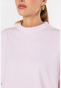 T-shirt en coton rose avec un col rond et des manches courtes. Présente un logo texturé "PEGADOR" dans une teinte de rose plus claire.