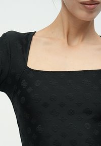 Μαύρο εφαρμοστό τοπ με τετράγωνη λαιμόκοψη και ανάγλυφα σχέδια σε όλο το ύφασμα, δημιουργώντας μια υφή με λεπτομέρειες.