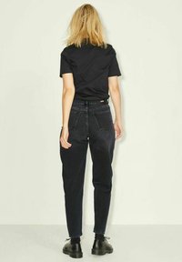 Jeans de mezclilla negra con un diseño de cintura alta y pierna ajustada. Combinados con una camiseta negra ajustada. Zapatos negros de tacón cerrado visibles.