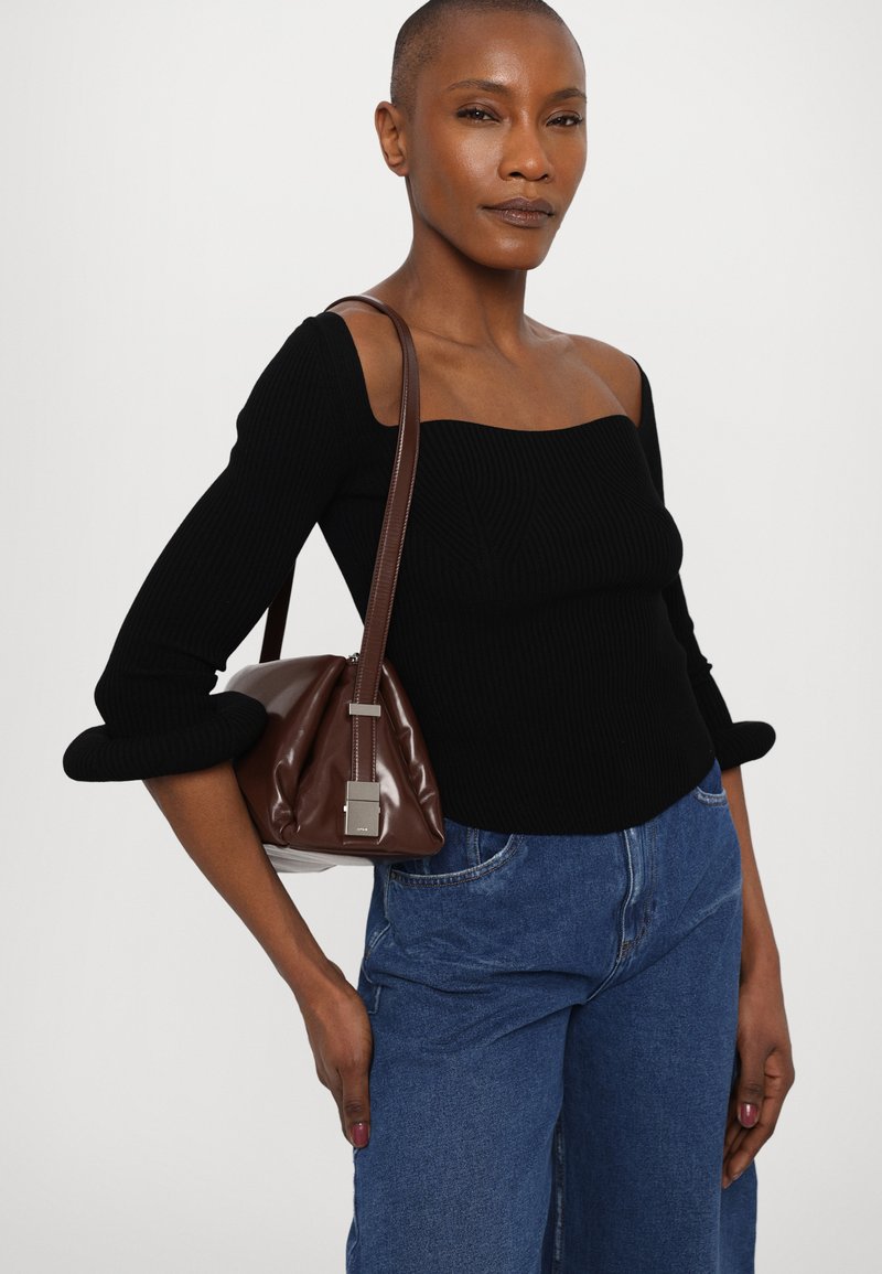 Top nero a costine con scollatura quadrata, abbinato a jeans azzurri a gamba larga e una borsa a tracolla in pelle marrone con un'accaento in argento.