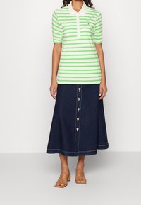 Green and white striped polo shirt with short sleeves, paired with a long, dark denim skirt featuring front buttons and a hemline finish.