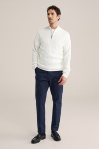 Weißer, gerippter Pullover mit Halbreißverschluss, kombiniert mit marineblauen Hosen. Schwarze Loafer vervollständigen das Outfit. Minimalistisches Design, entspannte Passform.