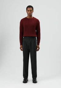 Bordeauxrode geribbelde trui met een ronde halslijn, gecombineerd met donkergrijze op maat gemaakte broek en zwarte schoenen. Soepele textuur en aansluitend ontwerp.