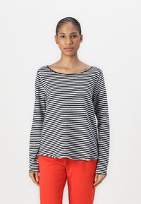 Stripet langermet skjorte i svart og hvitt, med bred hals og avslappet passform. Kombinert med røde slim-fit bukser.